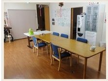 長テーブルに椅子が5脚並び、食器棚などが置かれた共有スペース