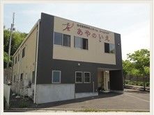 街路樹の並ぶ緩い傾斜地に建てられた、四角い2階建ての建物