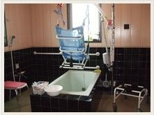 浴室には手動式入浴リフトが用意されている。浴槽の両脇には2脚の椅子、洗面器、シャワーなどがある。壁には手すりがある。