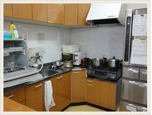 一般家庭にいるような収納スペースの多いキッチンである。大型の冷蔵庫や食器洗浄器、電子レンジが置かれている。