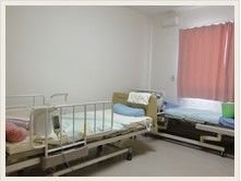 電動介護ベッドが二台置かれた居室である。ベッドには転落防止の柵が備わっている。窓にはカーテンがかかっている。