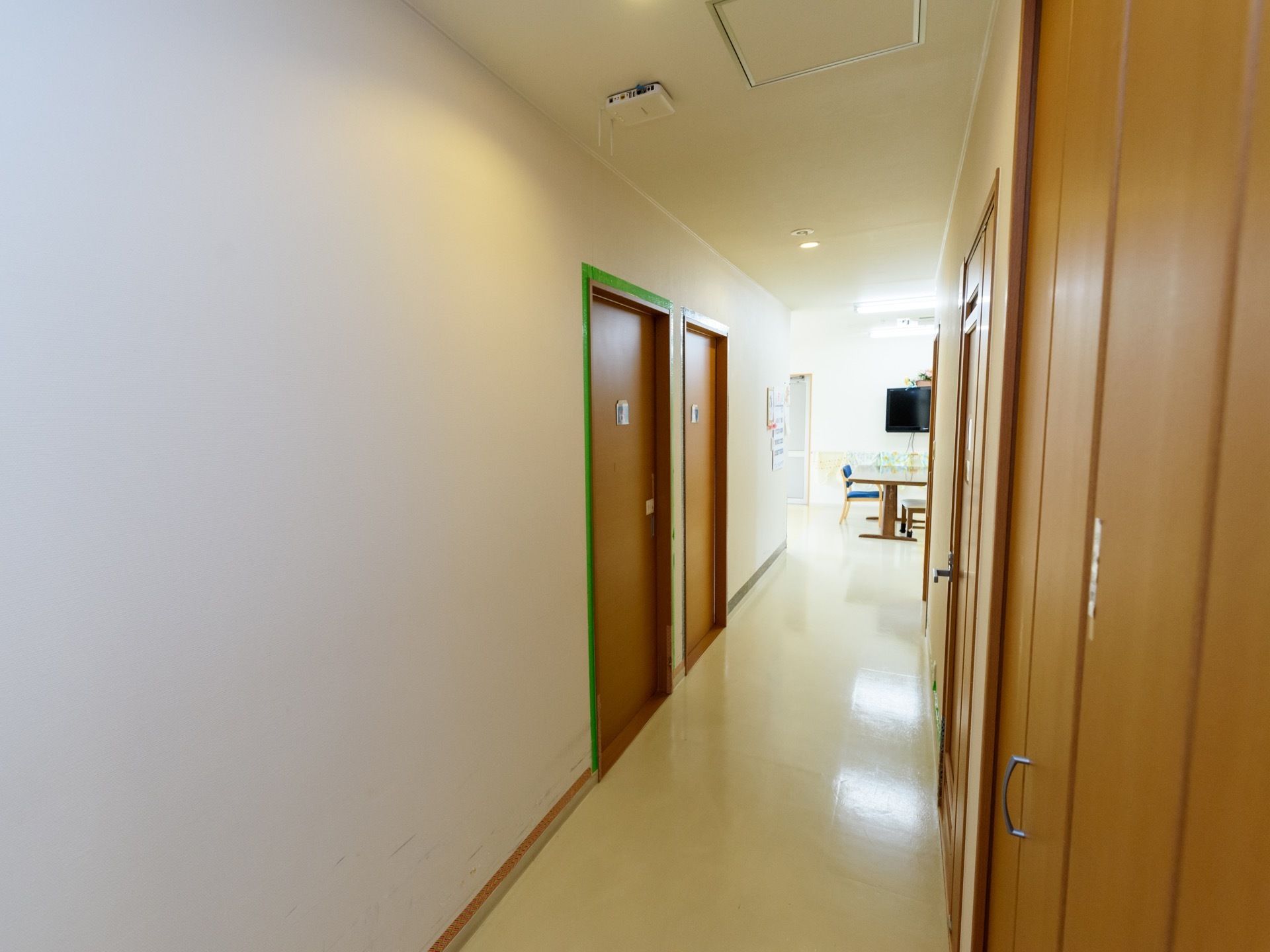 真っ直ぐな廊下には、居室やトイレのドアが左右にある。奥には、ダイニングテーブルやテレビが設置されている食堂がある。