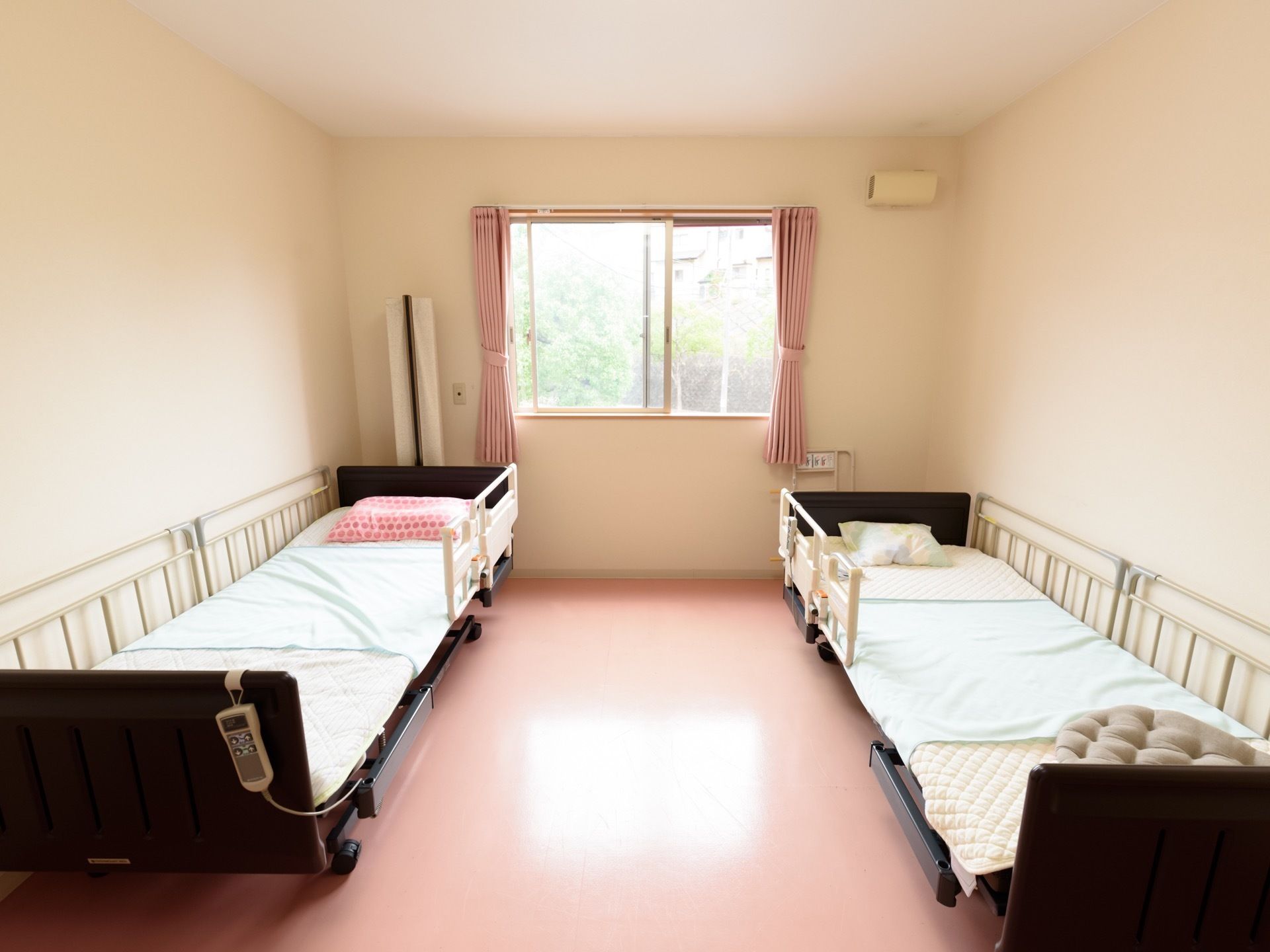 二人部屋タイプの居室である。２台の電動介護ベッドが置かれている。枕元の壁には、ナースコールが設置されている。