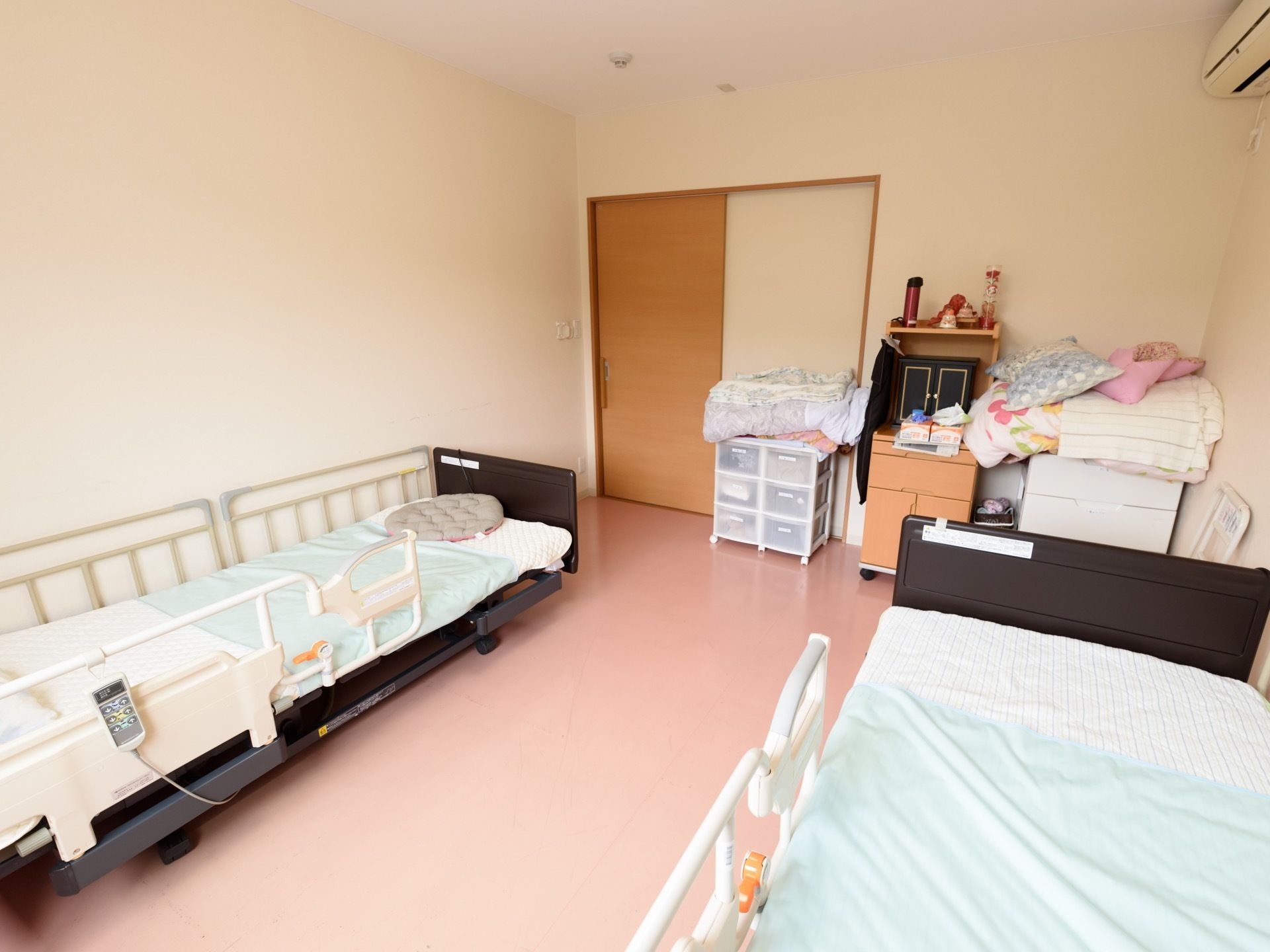 広めの間取りの二人部屋である。エアコンやナースコール、電動介護ベッドが完備されている。壁際に収納家具が置かれている。