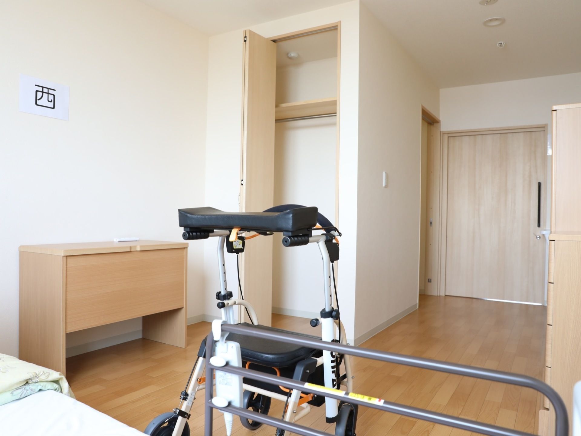 室内にはベッドを初め、歩行器や机、クローゼットなどがそれぞれ配置されている。クローゼットの右側に目を向けると、部屋の扉があるのがわかる。