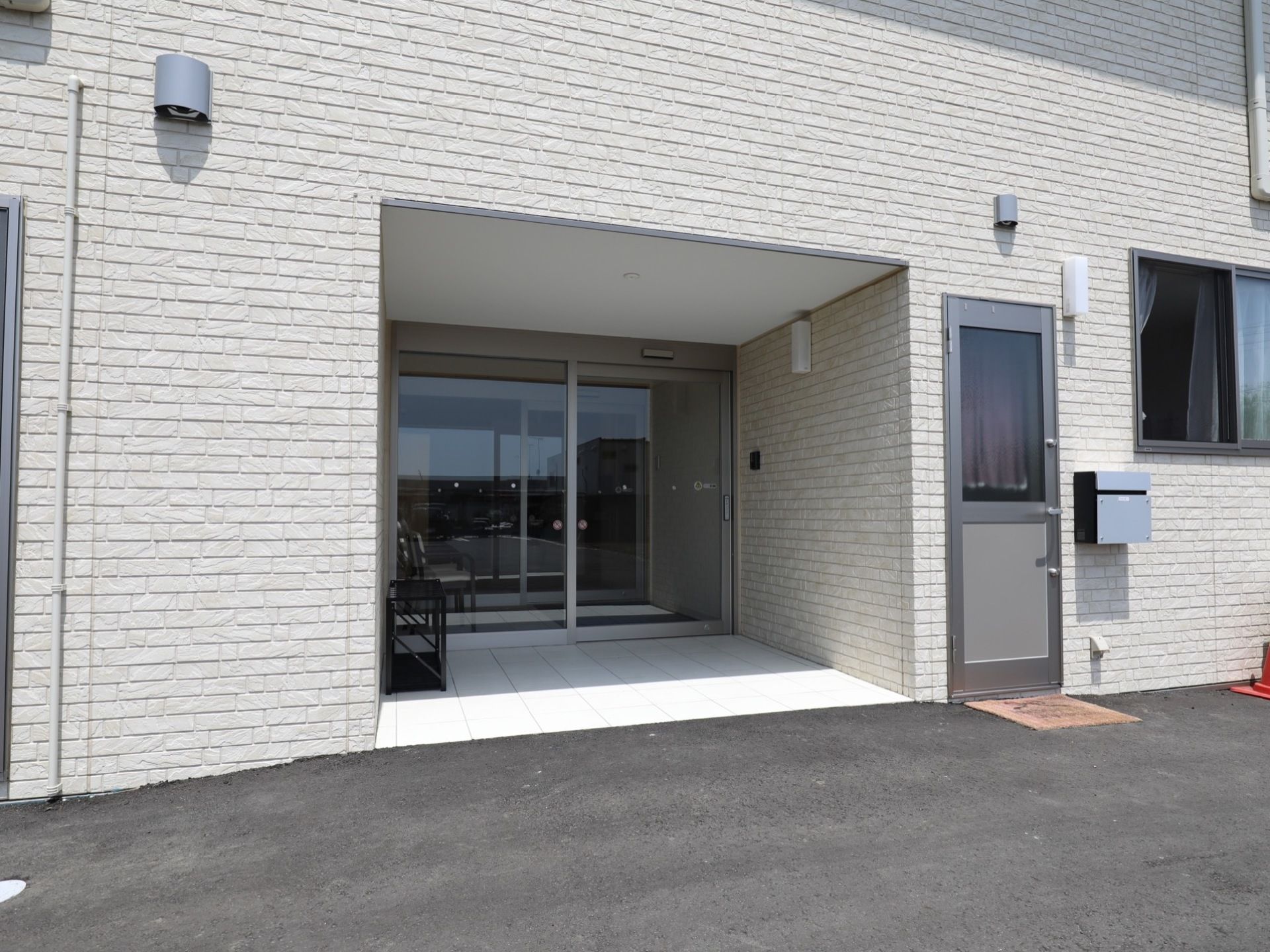 建物のへこんだ部分に入り口が設置されている。入り口は自動ドアになっており、片開き式のようである。入り口の手前には別の扉がある。