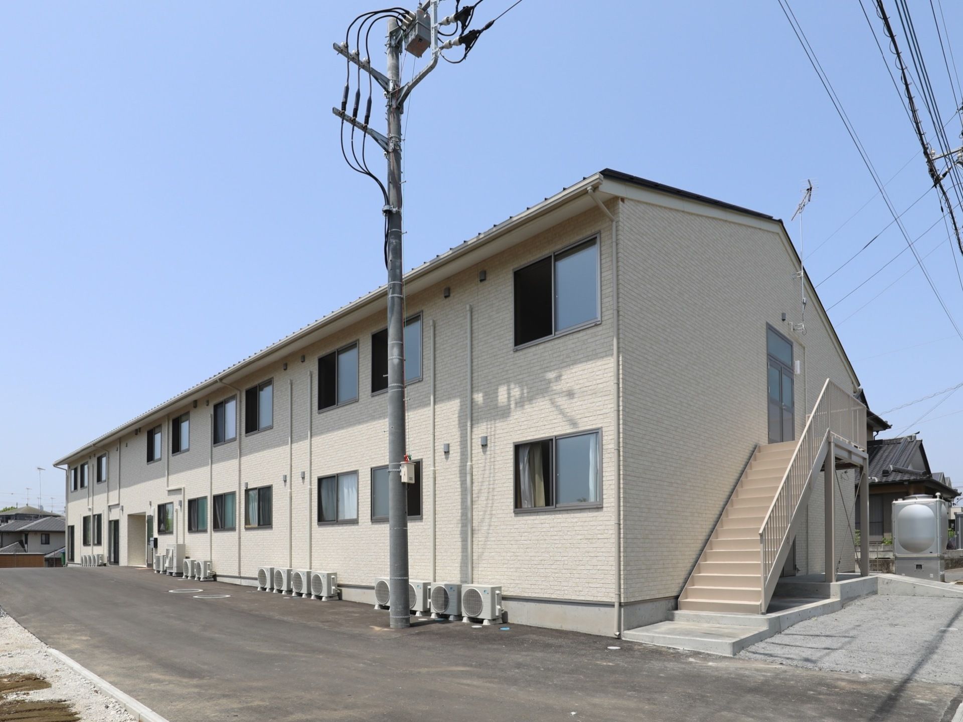 建物の正面側に電柱が建っている。施設の1階部分には換気用の機械が多数設置されている。2階の側面には階段が設けられている。