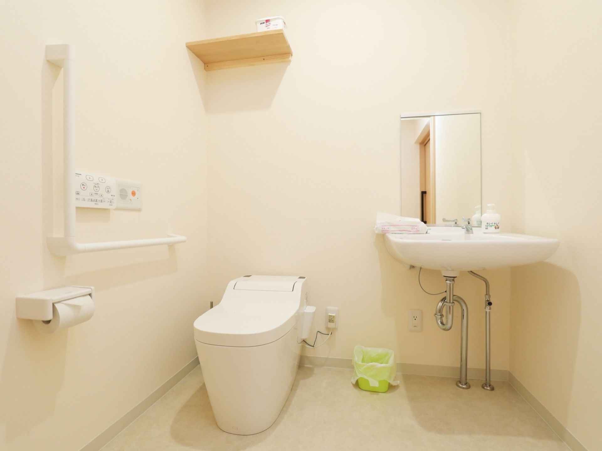左側に便座付き便器が設置されている。壁にはトイレ用ちり紙を支えるフォルダーが取り付けられている。右側には洗面台が設置されている。