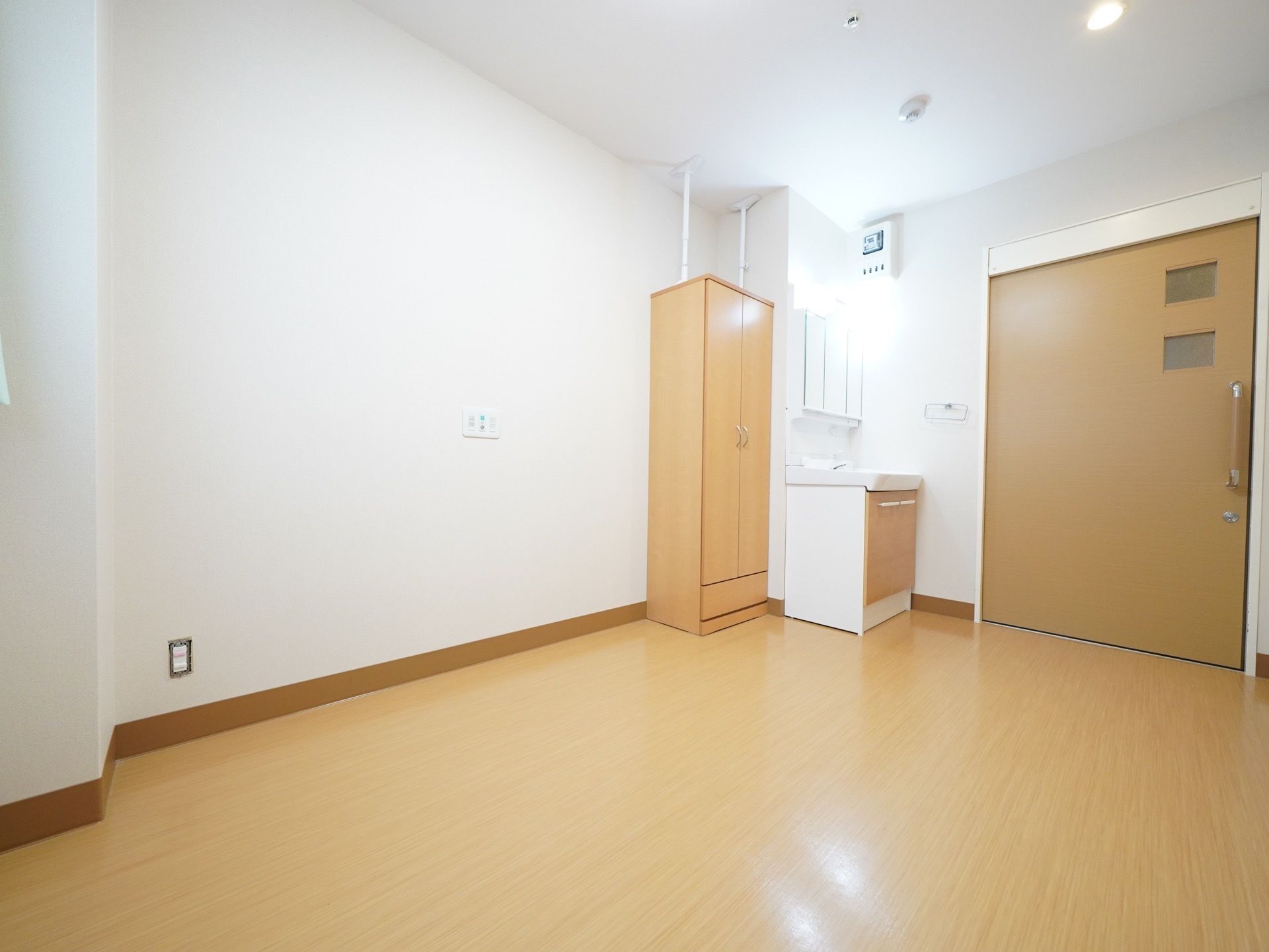 充分に広さを確保された居室。出入りしやすい大きな扉の造りになっており、近くには洗面台と衣類をしまう事のできるクローゼットが配置されている。