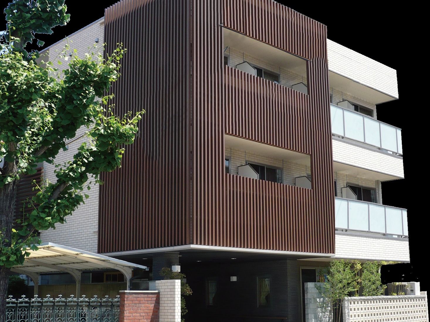 白と茶色の外壁で、1階には植栽がある3階建ての建物