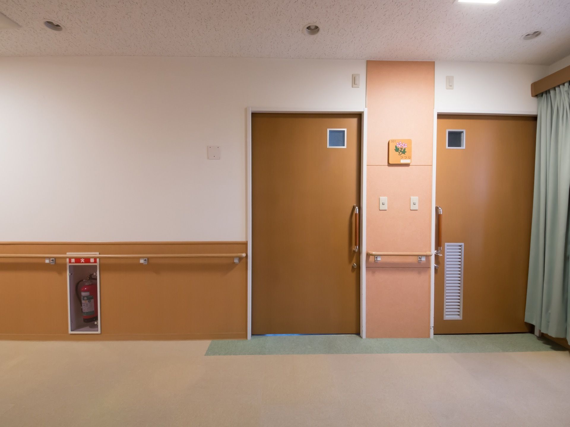 当施設の廊下の様子である。シンプルな落ち着きのある配色で、手すりやスライド式のドアなどのバリアフリー要素も備わっている。