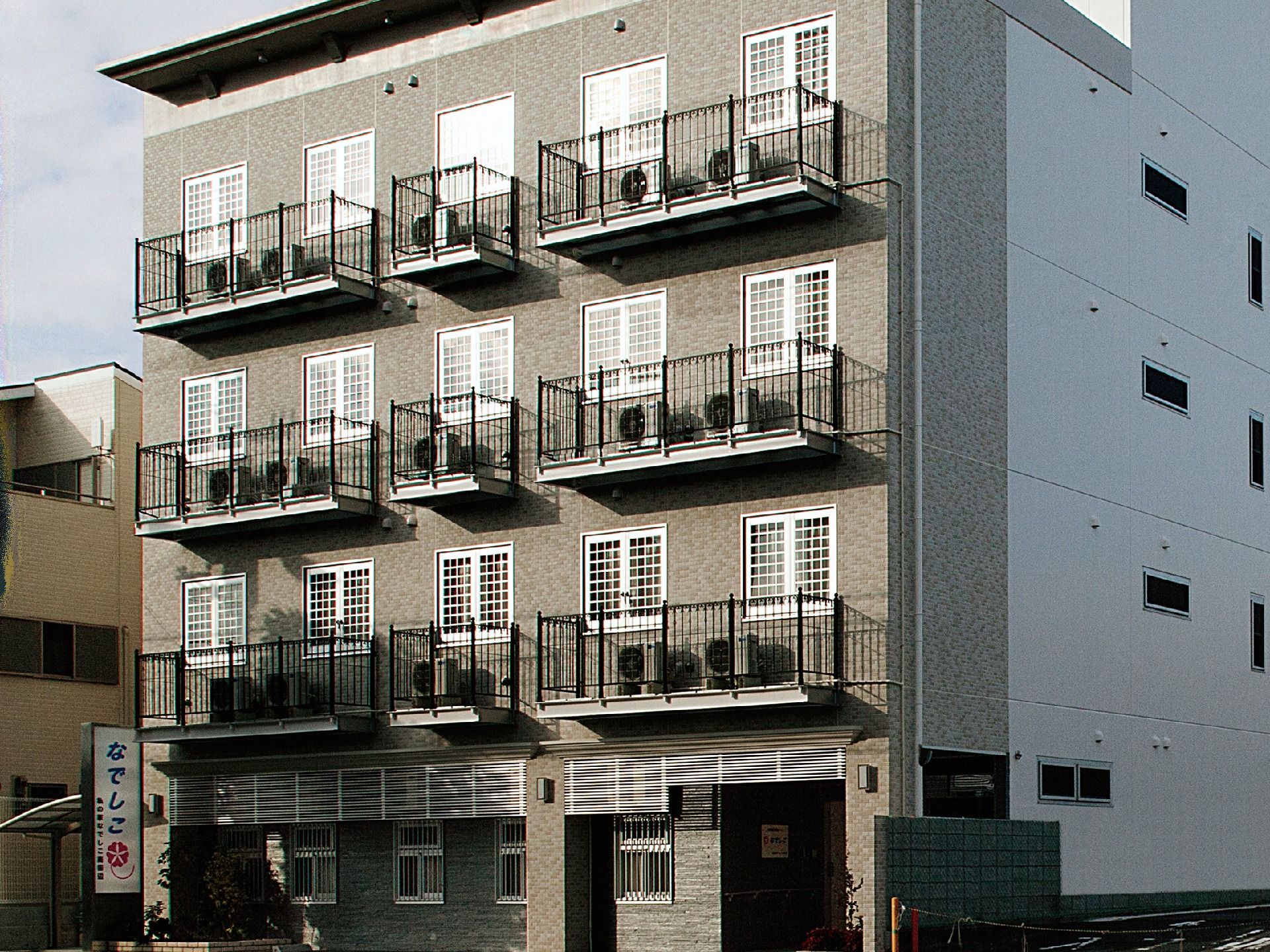 格子のついた四角い窓が、各階に5つ並ぶ4階建ての施設