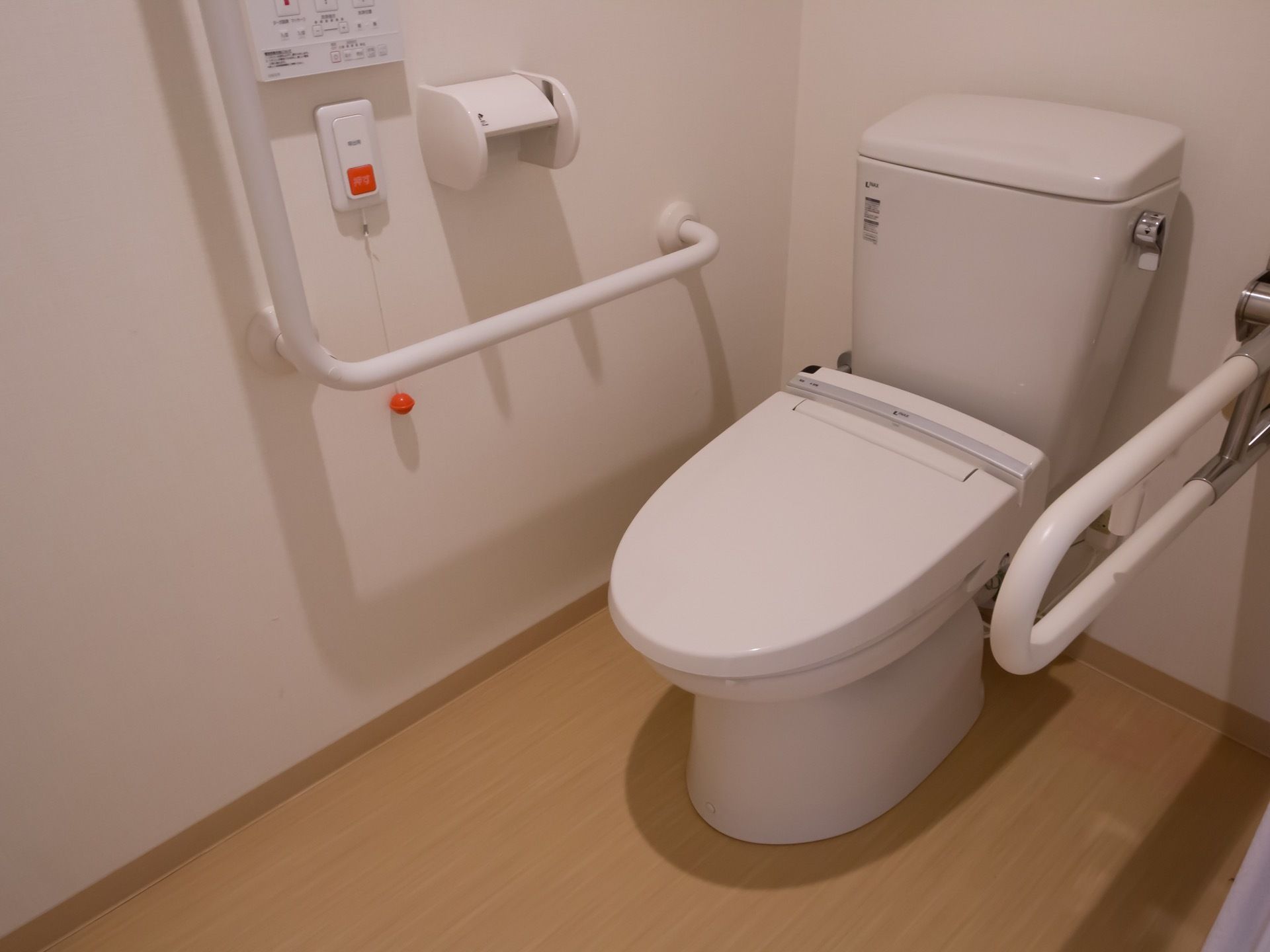 居室に、温水洗浄便座付きの個室トイレが用意されている。白い壁に、手すりとナースコールが設置されている。