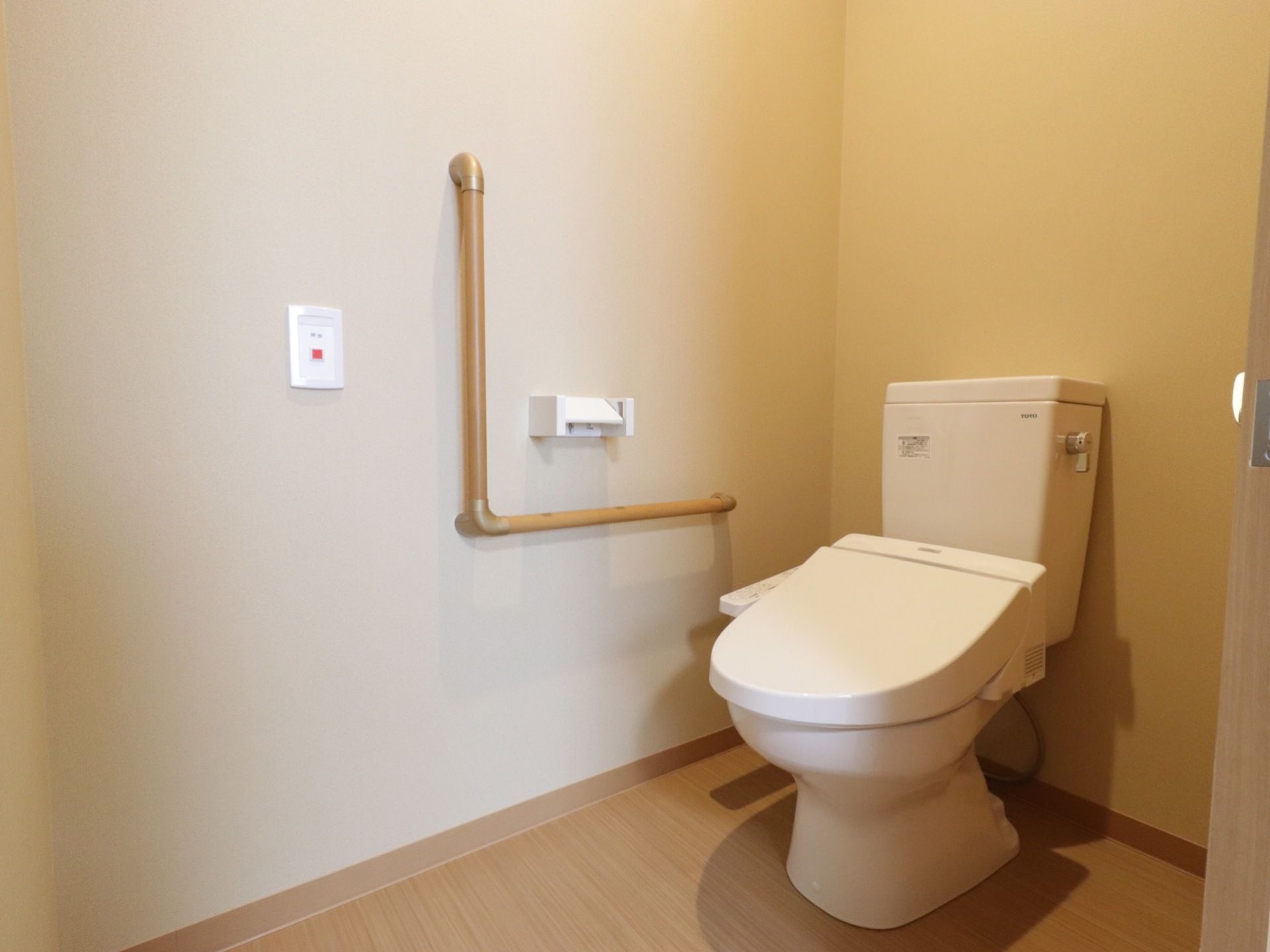 居室内に備わっているトイレである。L字型の手すりが備わっており、自立した便座への立ち座りをサポートしている。