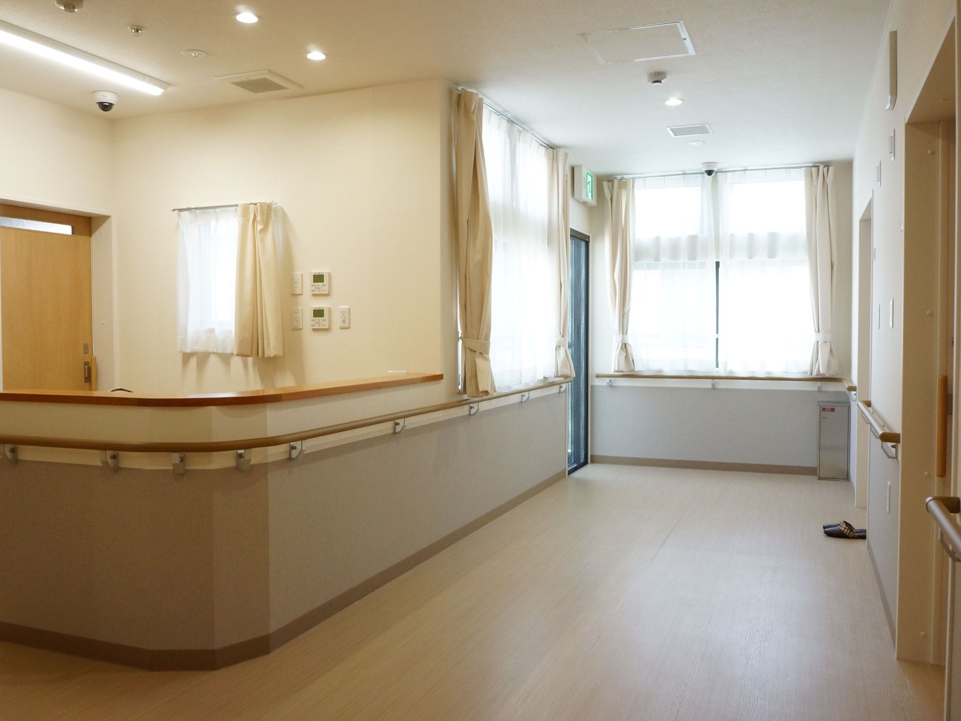 通路突き当りに非常口が見える。非常口の周囲は大きな窓がありとても明るくなっている。手前にはちょっとしたスペースが見える。