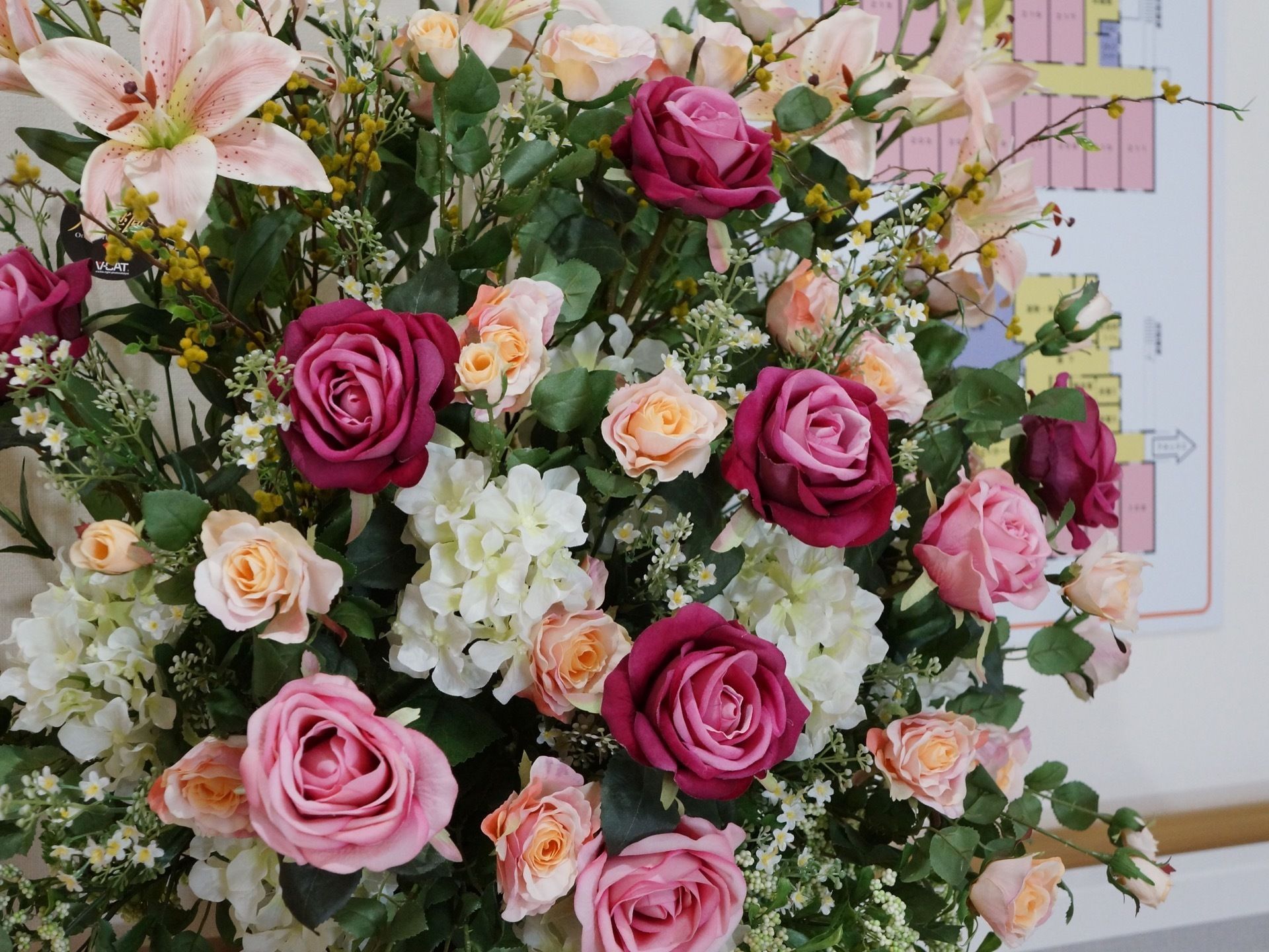 バラやゆりなど複数の花が混合して飾られている。色とりどりでボリュームがあり、華やかな印象を与えている。