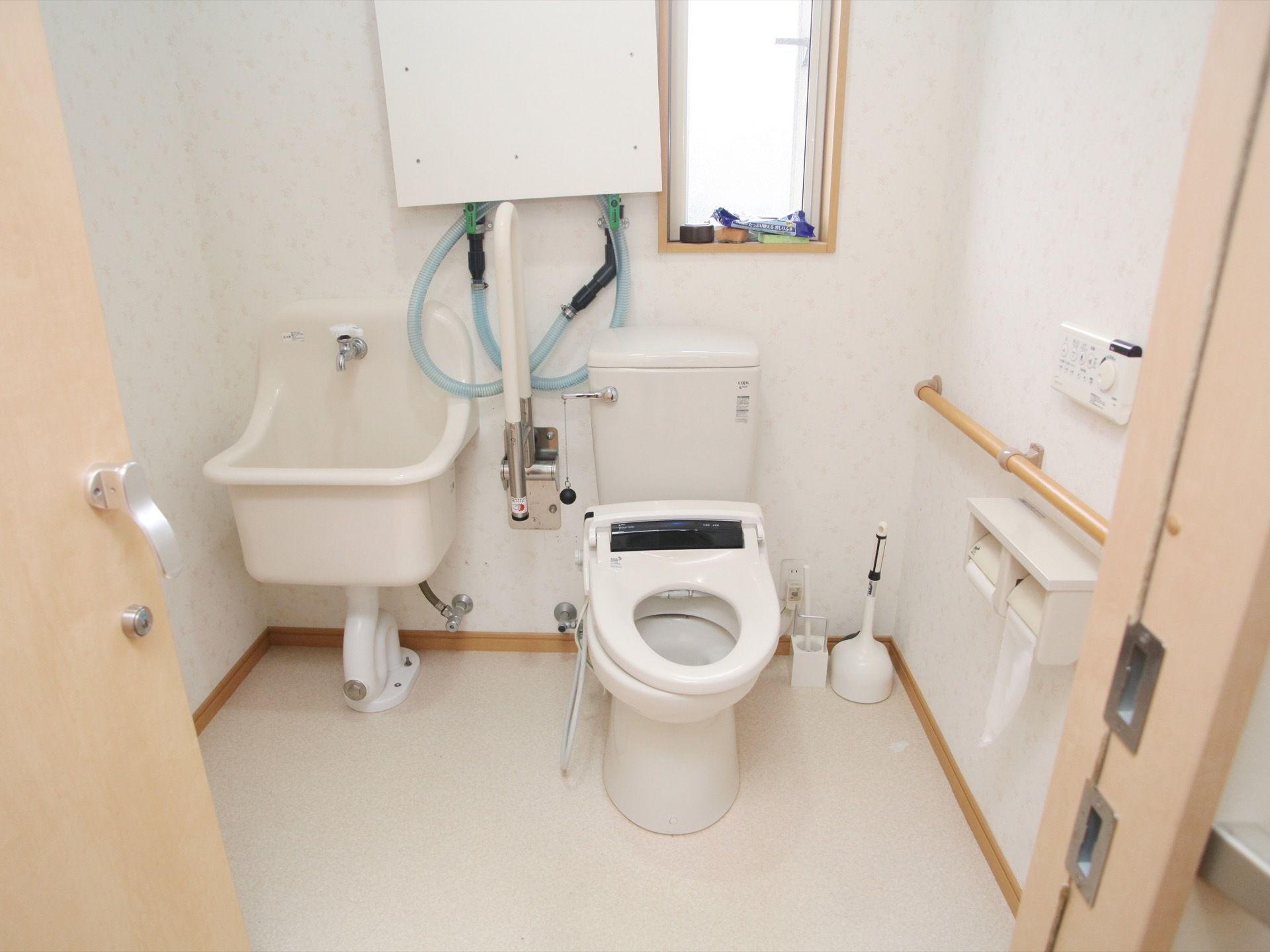 白を基調とした広々とした室内に便器と流し台が設置されている。壁には、手すりと温水洗浄機能のリモコンがある。