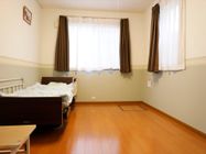 居室の床は木目調になっており、手すりのついたベッドが備え付けられている。小さめのテーブルが置かれている。