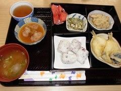 小さめのおにぎりと味噌汁、キスの天ぷらを主菜に副菜が３皿とデザートが、トレーに乗っている。飲み物はごはんに合わせてお茶が用意されている。