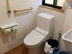 窓があり、外の光が入る明るいトイレである。壁に手すりを設置しており、立ち上がる際に体を支えることができる。