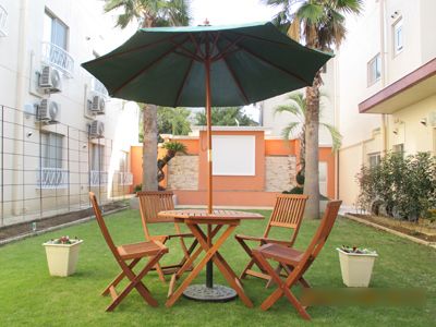 芝生敷きの床でヤシの木や植木があり、緑豊かな屋外の空間である。４脚の椅子とテーブル、パラソルがあり談話を楽しめる。