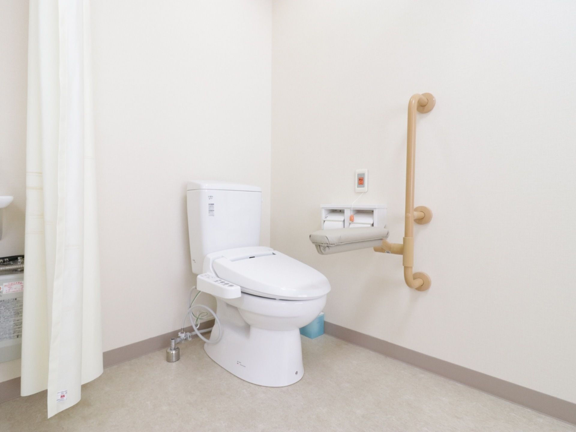 カーテンで仕切ることができる洗浄機能付きの洋式トイレである。壁には手すりと緊急呼び出しボタンがある。