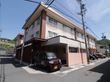 施設は路地の角地に建てられており、各部屋の窓には柵が設置されている。玄関前に施設の車両が止まっている。