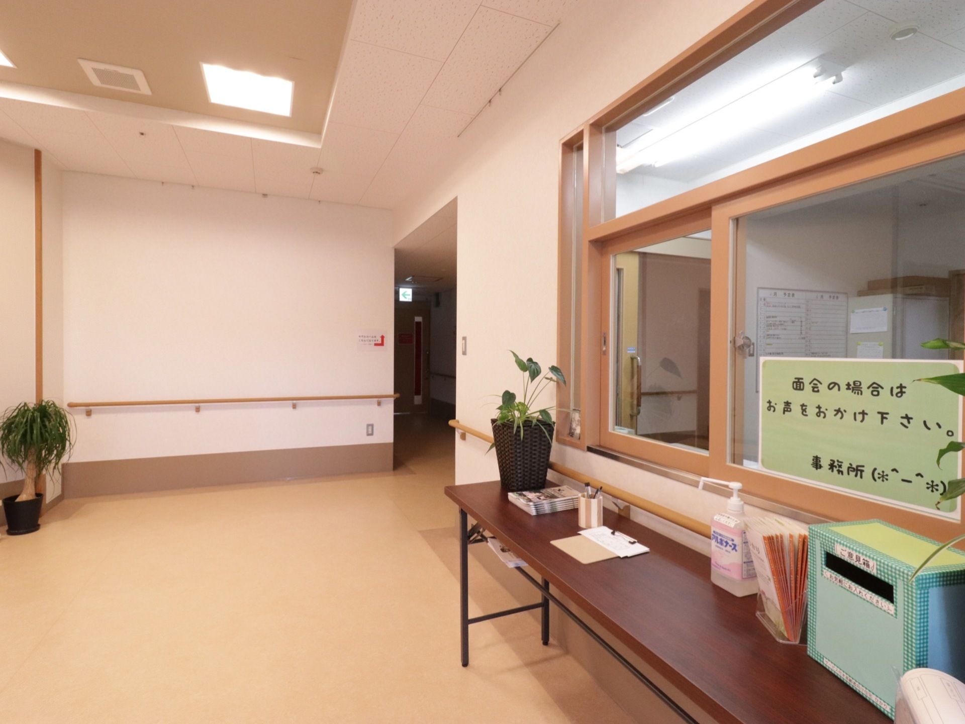 事務所の前に６尺机が置かれている。上には、受付表、鉛筆、パンフレット、ご意見箱、消毒液、観葉植物の小鉢などが乗せられている。
