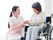 手を取り合う車椅子に乗った高齢女性と女性ヘルパー