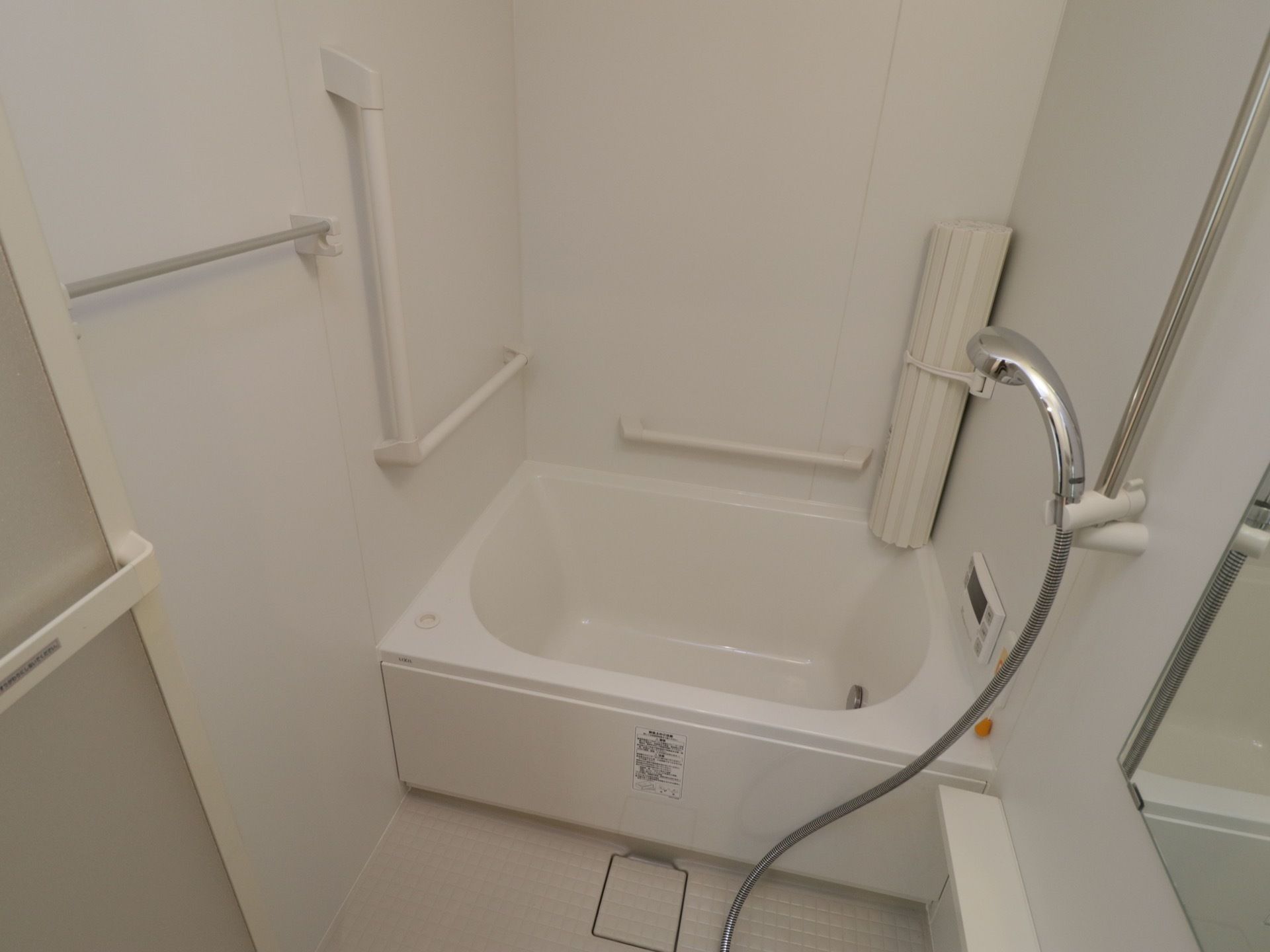 個浴用浴室の一例。白い浴槽があり、蓋が筒状に丸められて壁に立てかけられている。壁に操作パネルがある。
