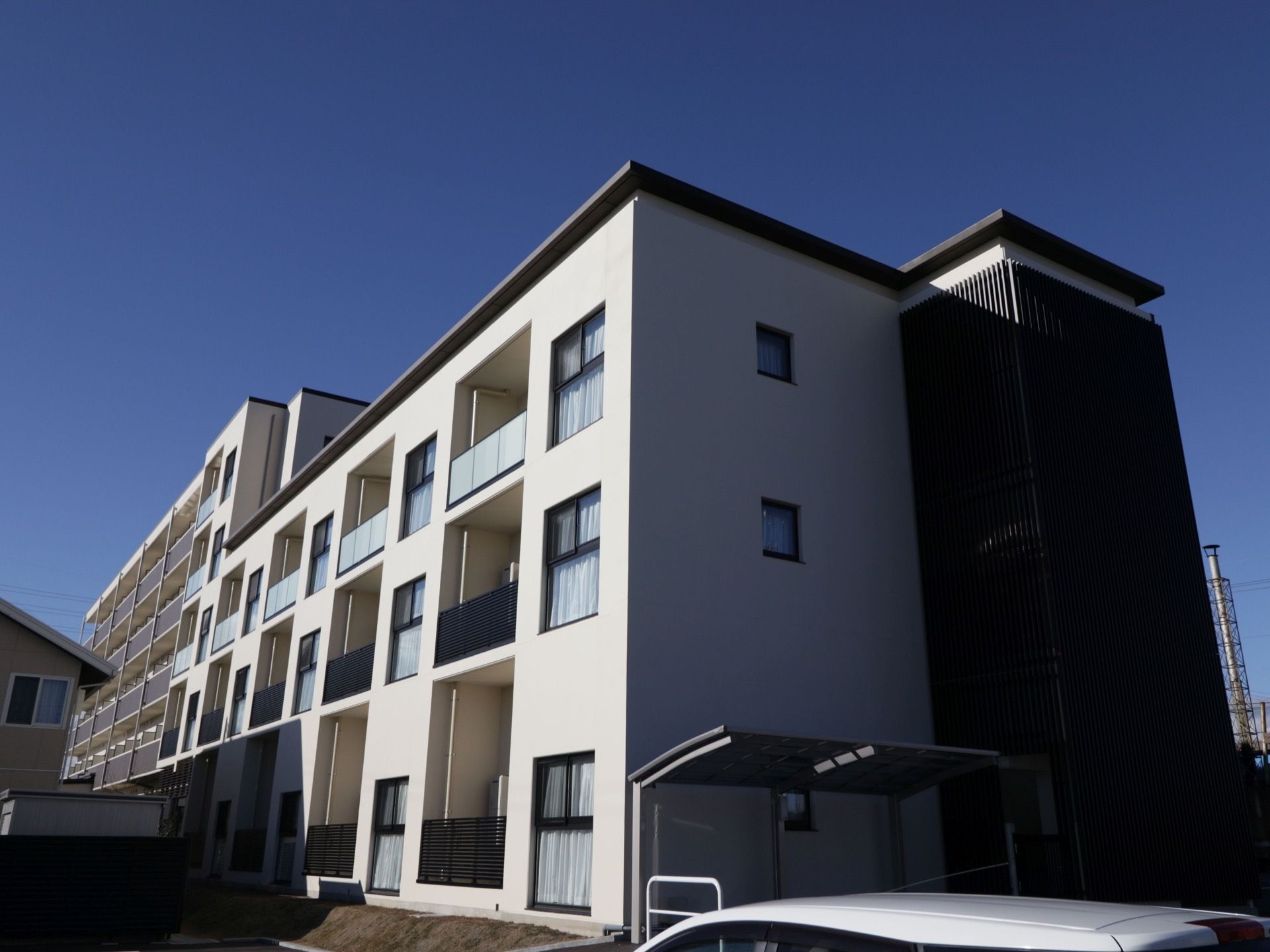 白と黒に塗り分けられた外観で、３階建てと５階建ての部分がある。外に自転車置き場があり、その手前が駐車場になっている。