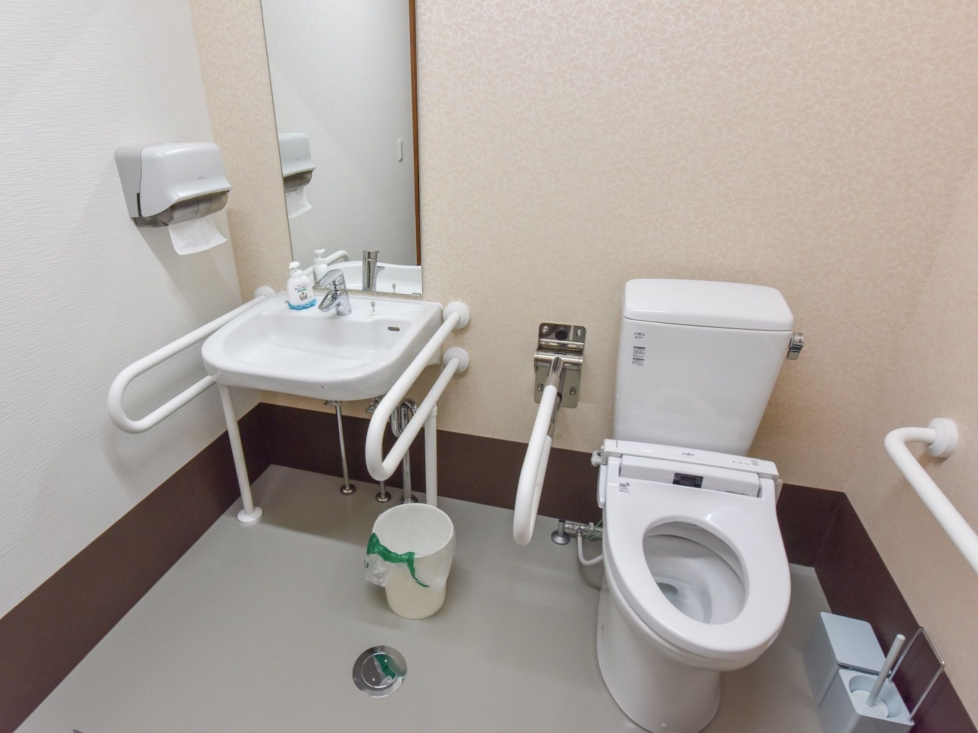 温水洗浄便座を使用している。掃除道具とゴミ箱が床に置かれている。洗面台の横にペーパーホルダーが設置されている。