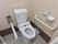 トイレは温水洗浄便座を採用しており、操作は壁面に設置されたパネルで行う。掃除用具が床に置かれている。