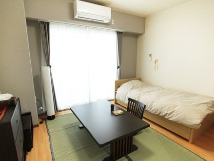 ベッド、座卓、座椅子などを置いて、ゆったりと過ごせるスペースのある居室である。大きな窓やエアコンもあり、快適である。