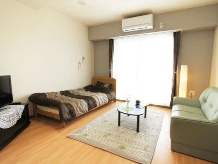 ベッド、ソファー、ローテーブル、テレビをゆったりと置くことができる。窓からの陽光が明るい部屋である。