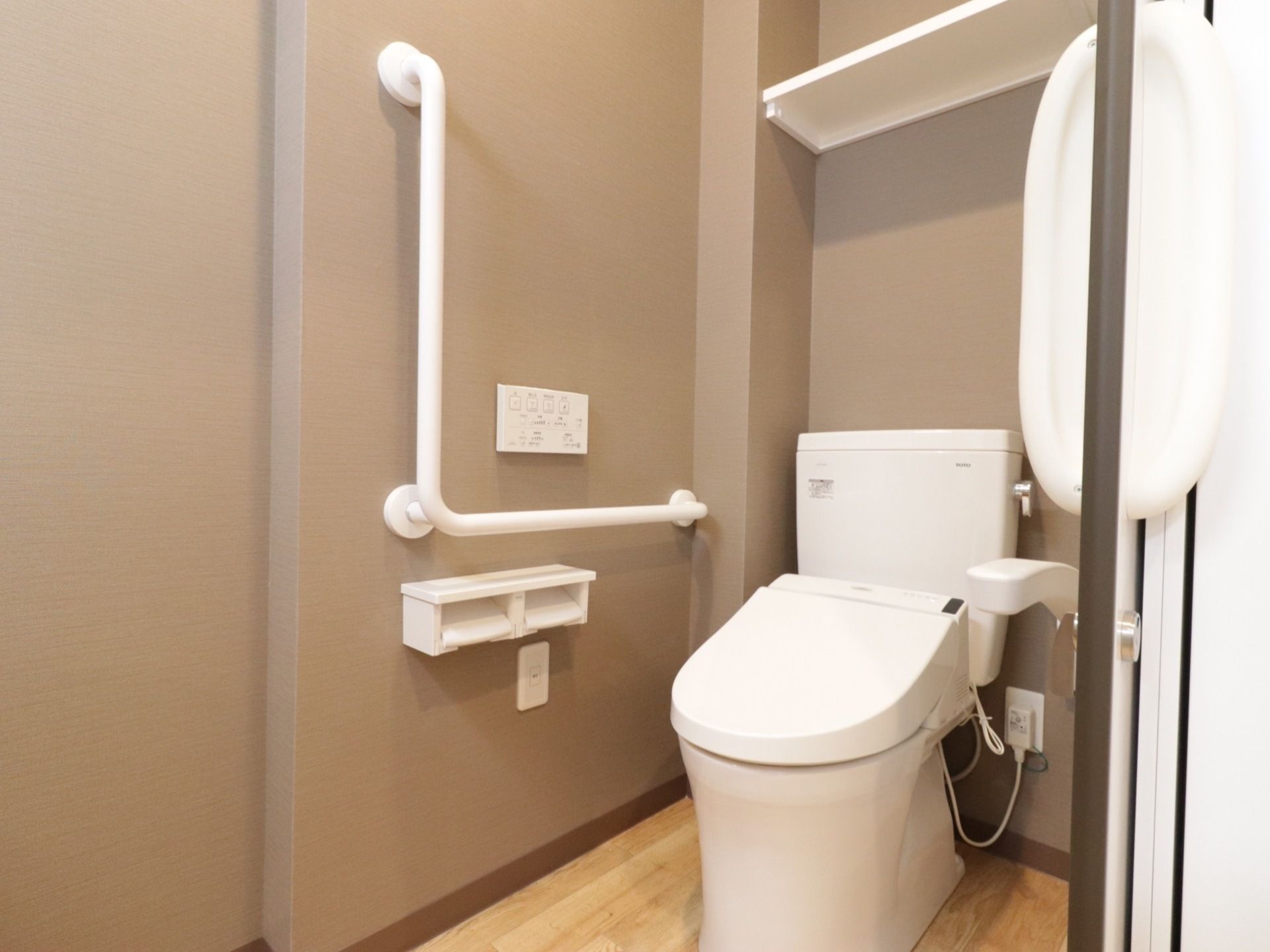 スライド式の扉になっているトイレには、温水洗浄便座が設置され、壁にはL字型の手すりが備えられている。
