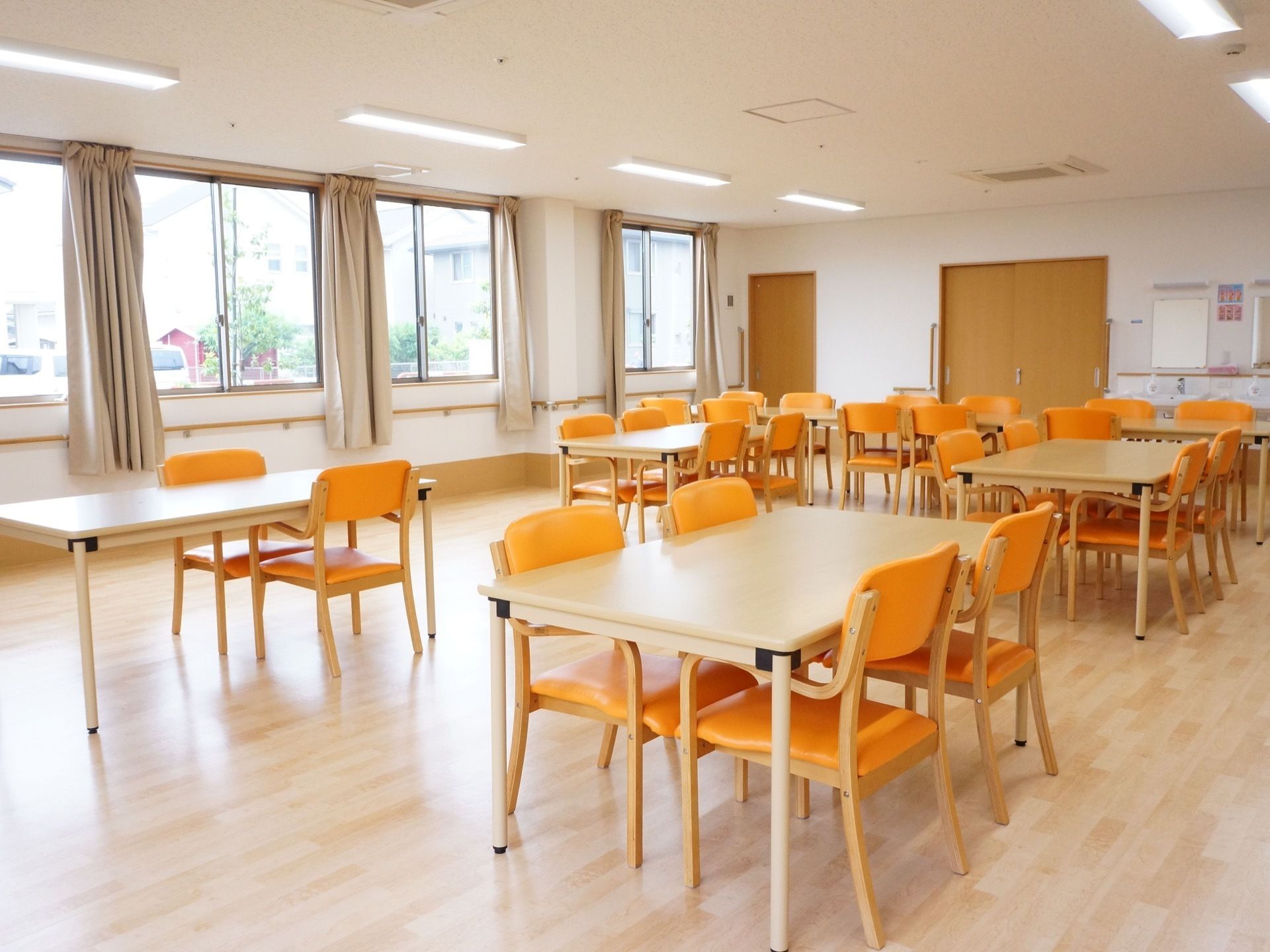 ベージュ色のカーテンが掛けられた数面の腰高窓から外の景色を見ることができる。壁には手すりが設置されている。