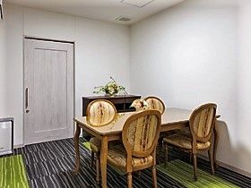 白い壁と扉、床はグレーとグリーンのコントラストがおしゃれな部屋。豪華な椅子が４脚、広々したテーブルが設置されている。
