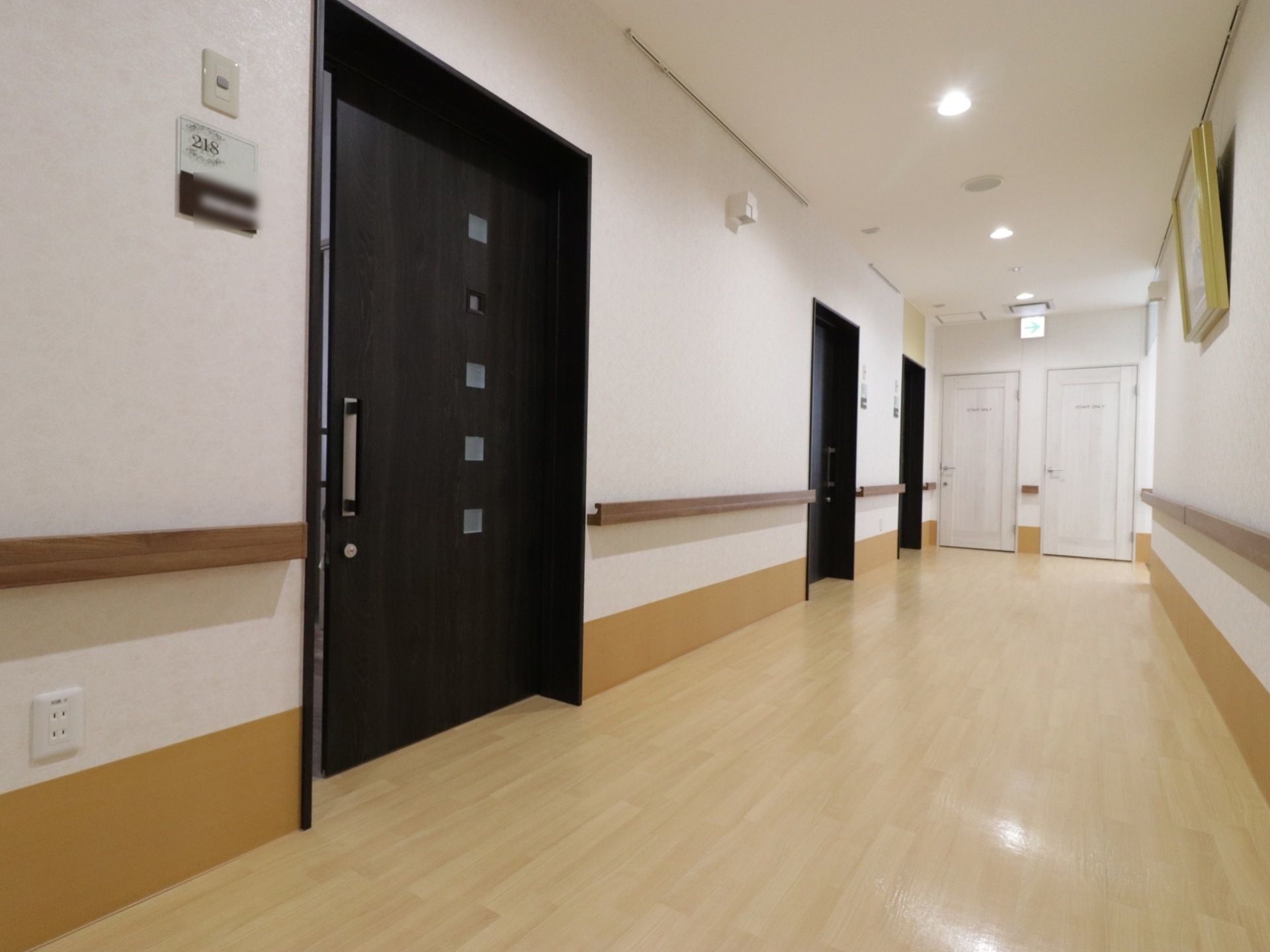 広々とした廊下には入居者様用の居室が並んでおり、扉は四角い小窓のついた黒い引戸が取りつけられている。