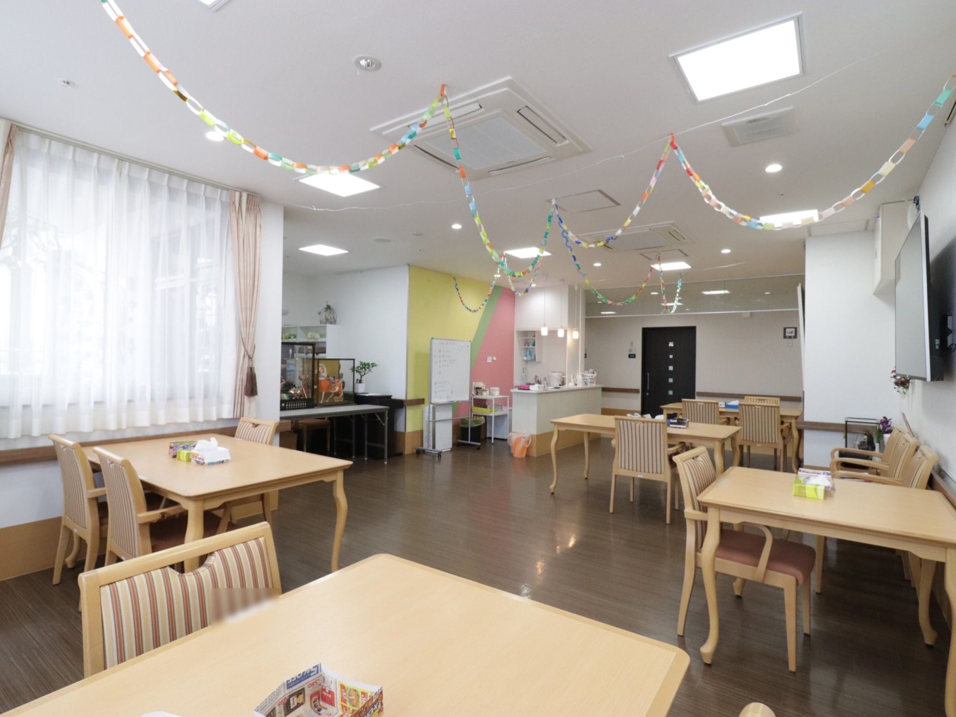 食堂にはテーブルと椅子がたくさん並んでおり、天井にはおりがみで作った輪飾りが飾られている。一角には、ケースに入った人形が飾られている。
