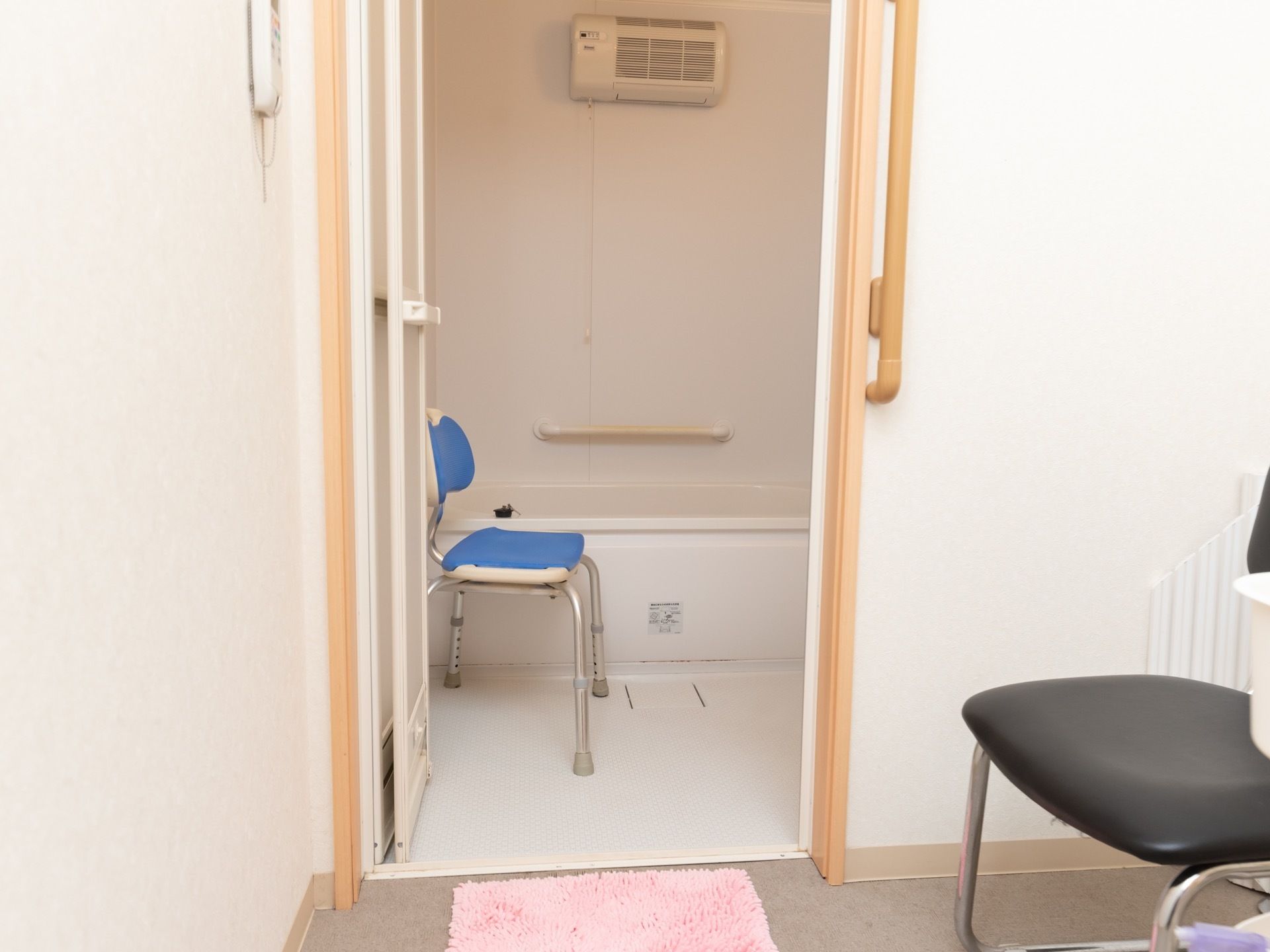 個室用の浴槽が用意されている。洗い場には背もたれ付きのシャワーチェアが置かれている。脱衣所にはバスマットが敷かれている。