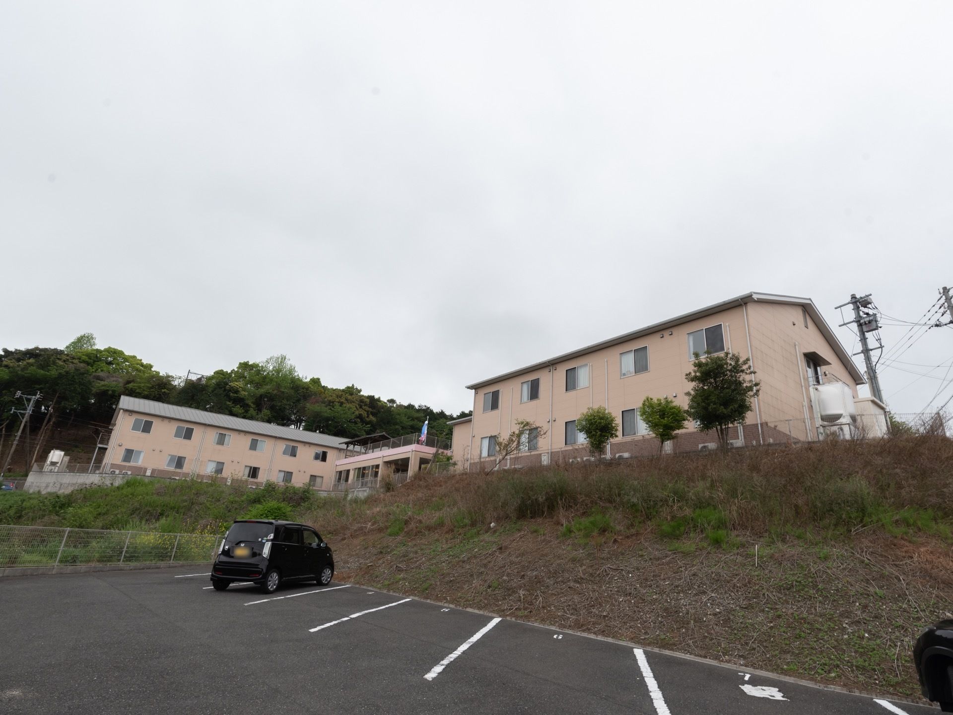 ベージュ調の2階建ての建物である。敷地内には広々とした駐車場が完備されており、車が1台停まっている。