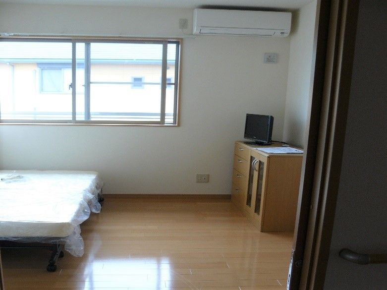 フローリング仕様の個室タイプの居室。ベッドや収納家具、テレビが置かれ壁にはエアコンが設置されている。