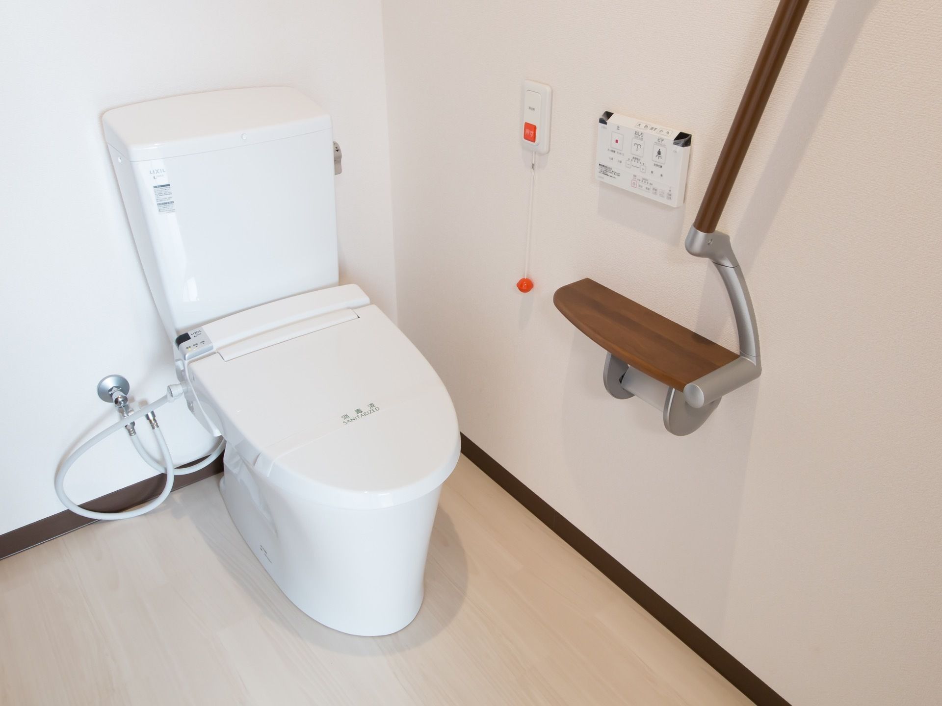 濃いブラウンの、可動式の手すりが備わっている。トイレは温水洗浄便座で、ナースコールも設置されている。