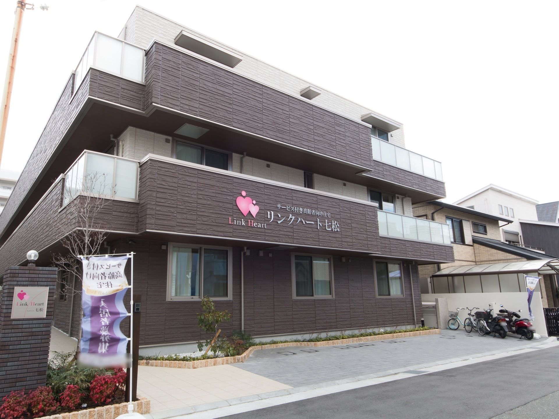 道路に面した場所に位置する３階建ての施設である。敷地内に庭木を植えるなど、緑地がきれいに整備されている。