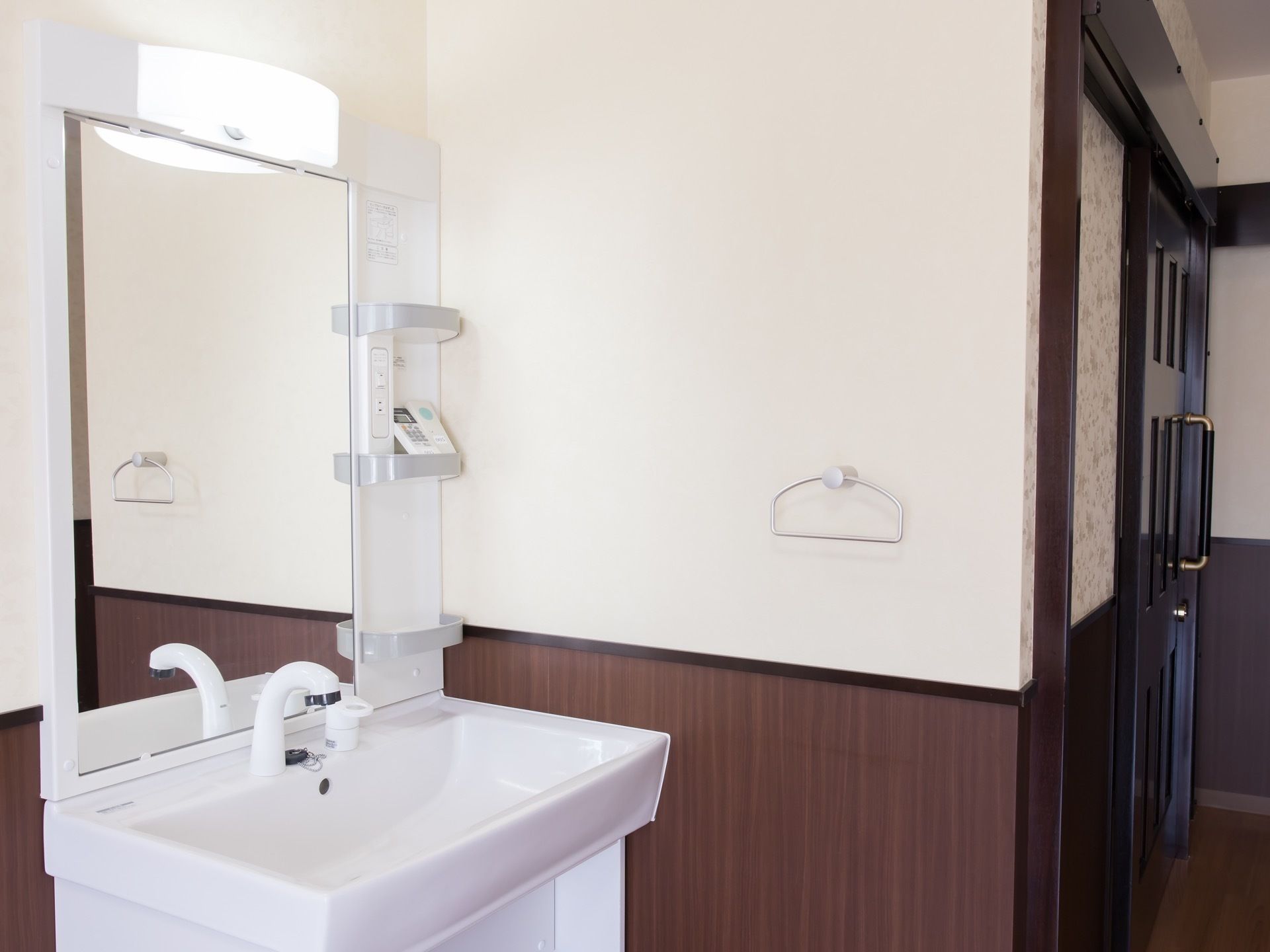 居室に備え付けられた洗面台の画像である。右奥は廊下に続いており、トイレの扉が見えている。左手前に洗面台がある。