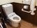 床と壁が木目調のトイレである。中央に温水洗浄便座が取り付けられた洋式トイレがある。壁に手すりが取り付けられている。