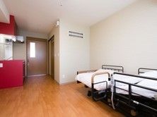 左手にキッチンスペースがある、部屋の奥には電動のベッドが設置されている。床はフローリングで段差のない造りになっている。