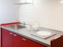 個室のキッチンは赤紫色の華やかな印象である。コンロはIH仕様で、火を使わないため安全である。キッチンは広いスペースを確保している。