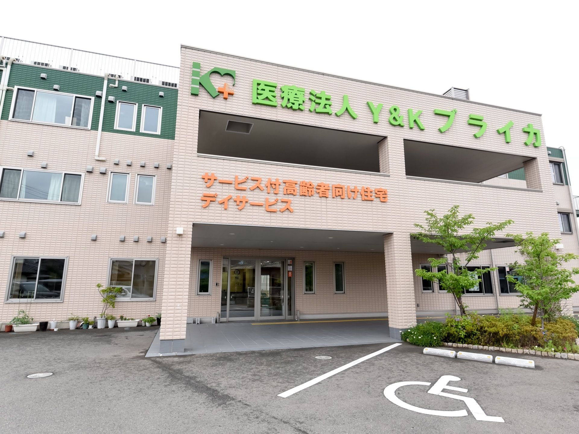 ３階建ての建物である。施設名が外壁に大きく記されている。エントランス前には、介護車両の駐車スペースが設けられている。